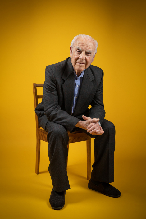 Distinguished senior gentleman portrayed in an in-studio portrait, seated on a chair exuding a sense of poise and wisdom.