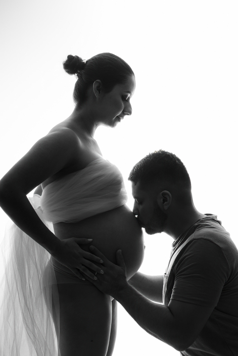 Intimate in-studio moment: Husband tenderly kissing the tummy of his pregnant wife, expressing love and anticipation.