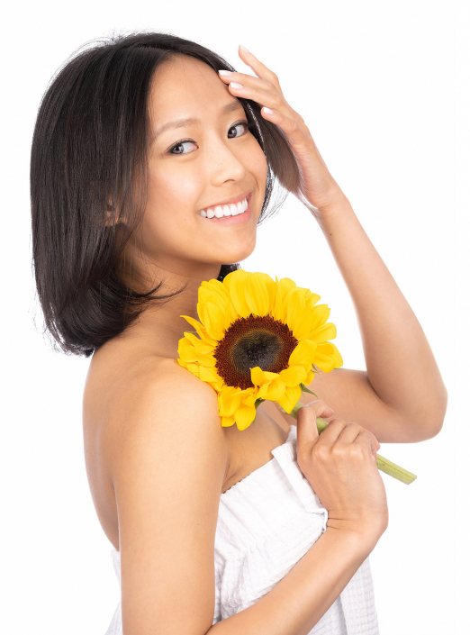 Headshot of radiant woman with a smile, poised for a spa experience, holding a sunflower.