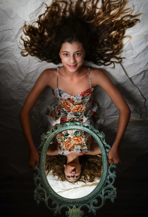 Imaginative in-studio capture: Teenage girl engrossed in playful interaction with her mirror reflection, expressing creativity and self-expression.