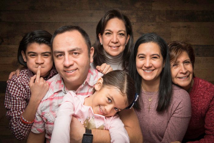 Warm Latin family portrait captured in a studio setting against a rustic wooden backdrop.