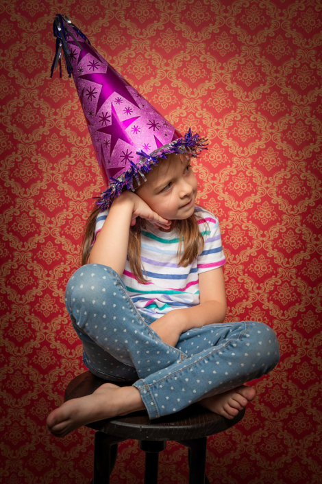 Joyful girl celebrating her birthday, seated on a stool against a festive red backdrop.