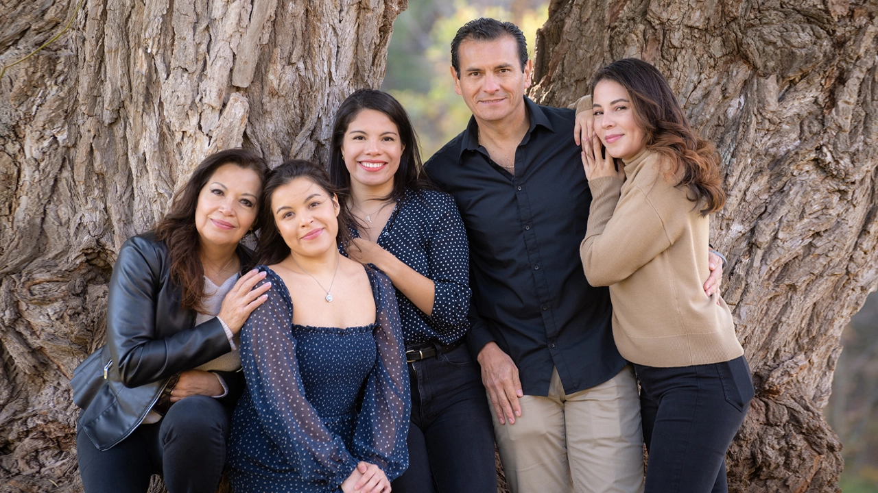 Hispanic family at Sixteen Mile Creek, standing in front of a picturesque tree.