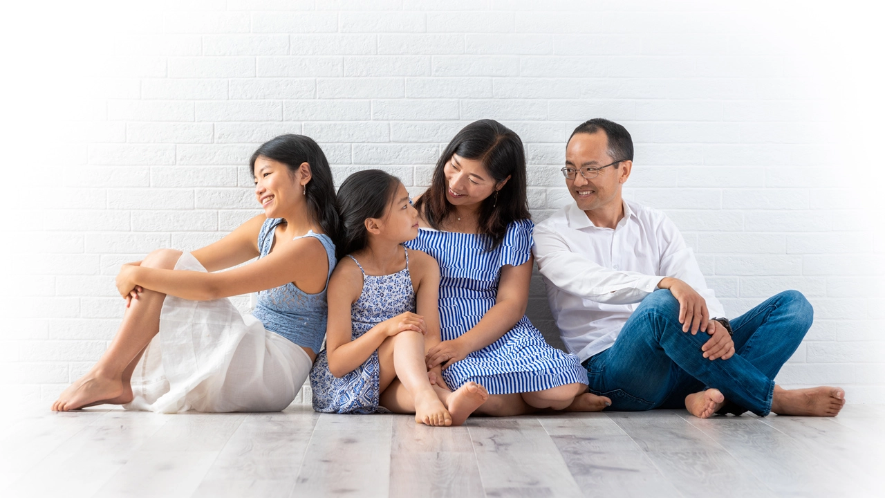 Indoor gathering of an Asian family, seated on the floor with brick wall backdrop, featuring blue accents.